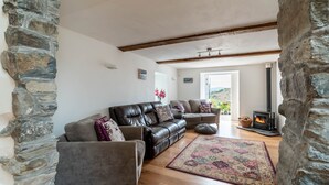 A cozy living room with a stone wall, a leather sofa, a rug, and a fireplace. - Bryn Eithin Cottage Far From the Madding Crowd (Corwen)