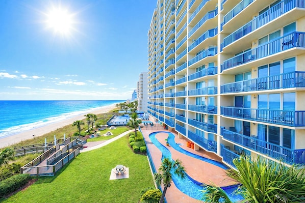 A hotel with a pool, a beach view, and a large building with balconies.