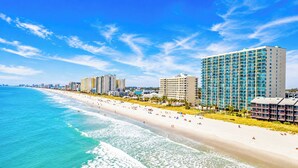 Un hotel frente a la playa con varios edificios altos, una playa de arena y el océano.