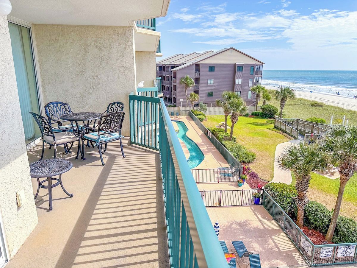 Un balcón con mobiliario exterior, una piscina y vistas a la playa y al océano.