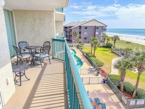 A balcony with outdoor furniture, a pool, and a view of the beach and ocean.