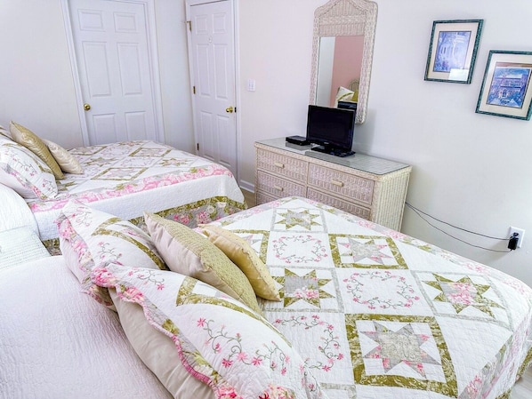 A bedroom with two beds, a dresser, a mirror, and framed pictures on the wall.
