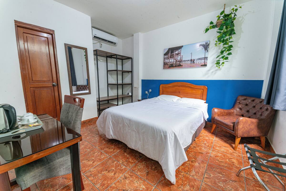 Una habitación de hotel con una cama, un escritorio con silla, un espejo y una estantería en la pared.
