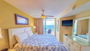 Habitación de hotel con cama, televisión, cómoda y balcón con vista al océano.