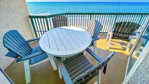 Un balcón con una mesa redonda y cuatro sillas Adirondack, con vista a una playa y el océano.