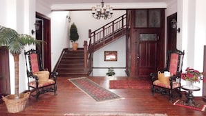 Ein geräumiges Foyer mit einer Holztretreppe, zwei verzierten Sesseln, einer Kristallleuchtre und einem roten Teppich.