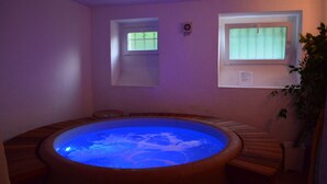 Ein Whirlpool mit blauem Licht, Holzbänken, einem Fenster und einer Pflanze.