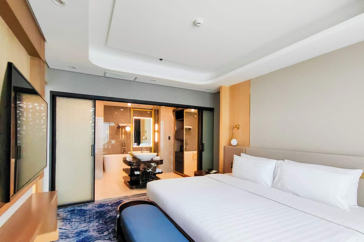 Ein Hotelzimmer mit einem großen Bett, einem Nachttisch, einem Spiegel und Blick auf das Badezimmer.