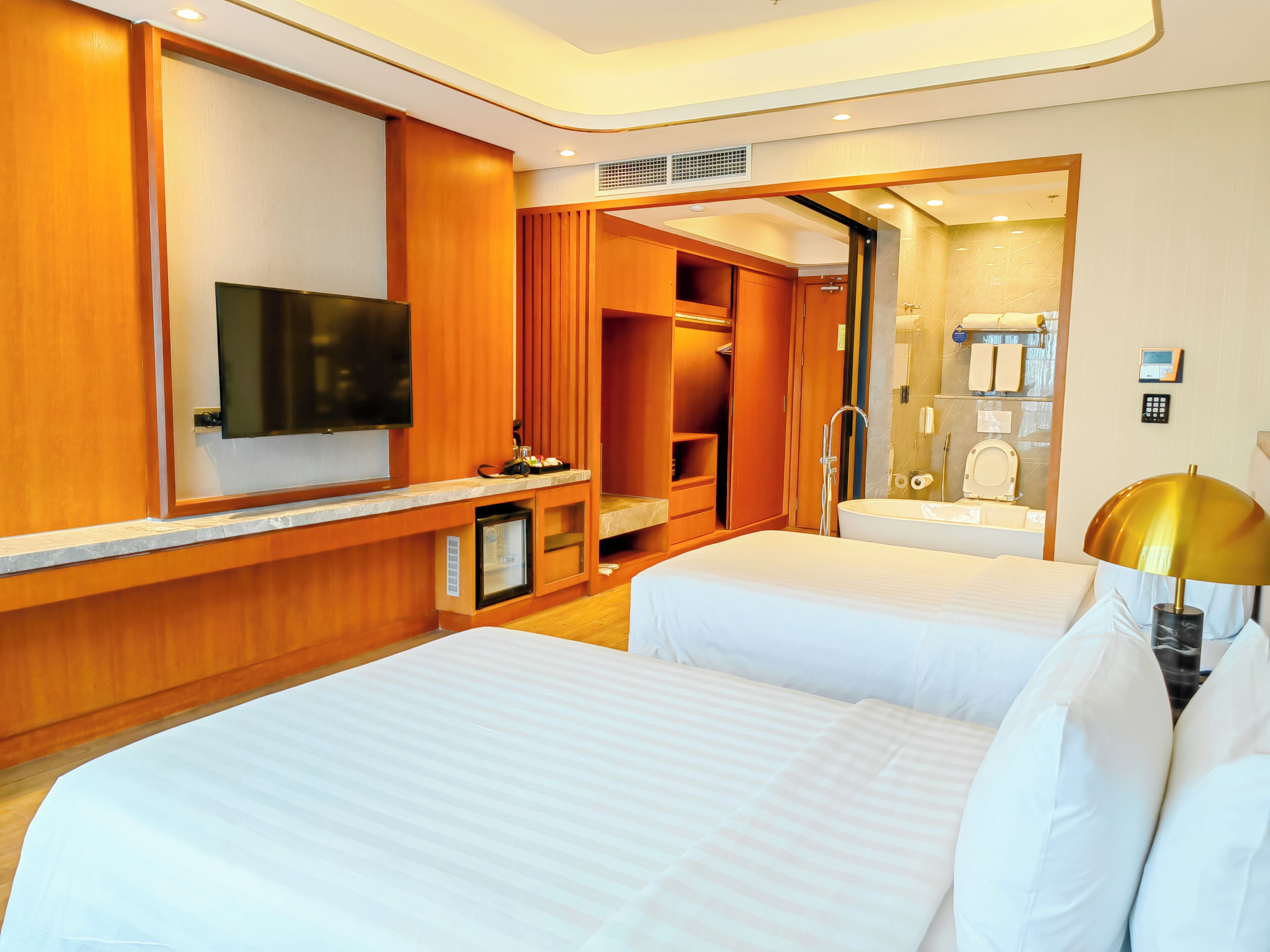 Habitación de hotel con dos camas, televisión, minibar, zona de ducha y baño con lavamanos e inodoro.