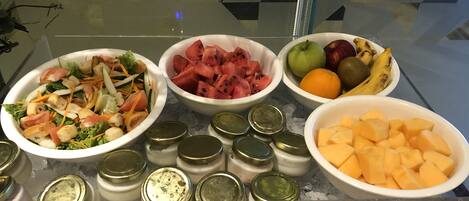 Un buffet proposant divers plats, notamment une salade, de la pastèque, des fruits et du fromage.