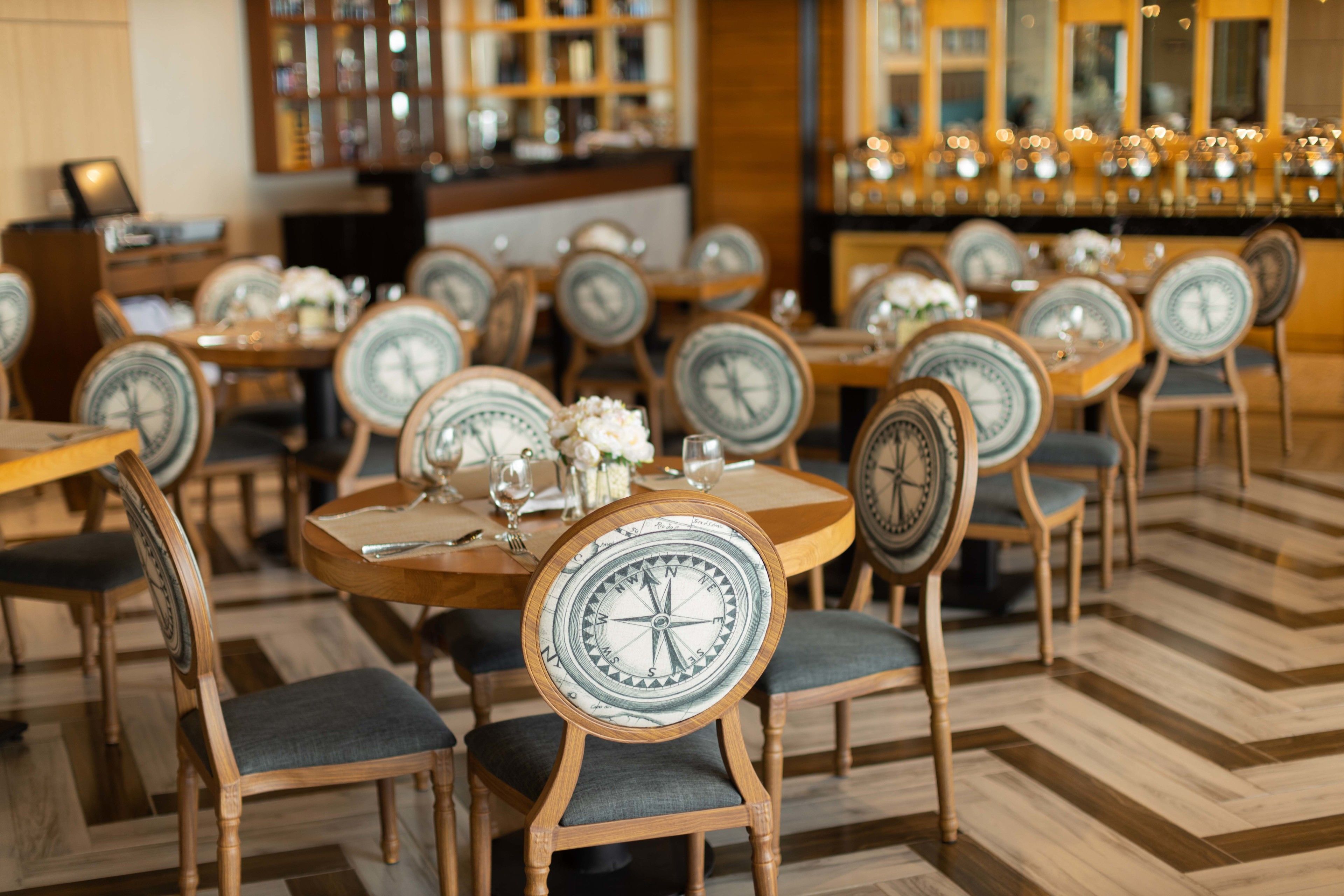 A restaurant with round tables and chairs, each with a compass design on the backrest.