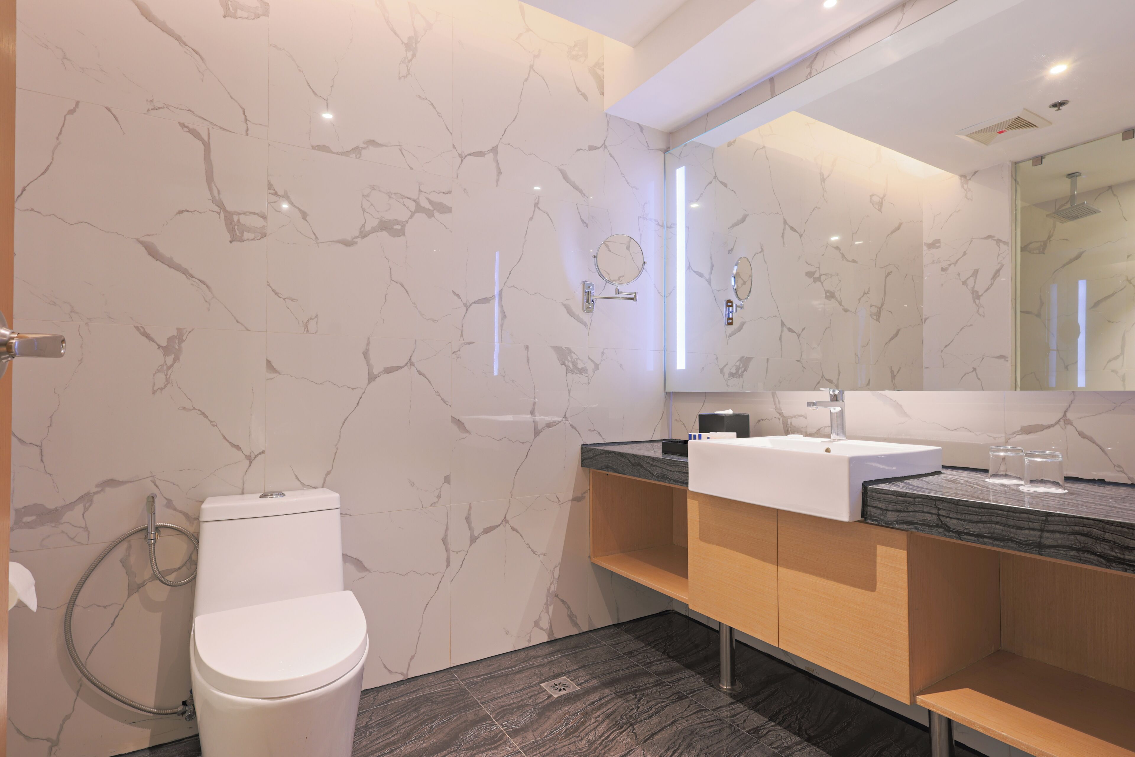 Une salle de bain moderne avec des toilettes blanches, des murs en marbre, un lavabo noir et un meuble-lavabo en bois.