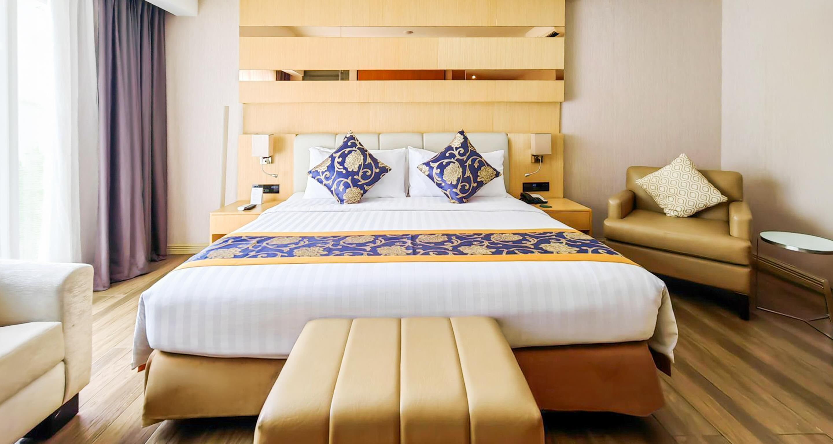 A hotel room with a large bed, a sofa, a small table, and a bench.