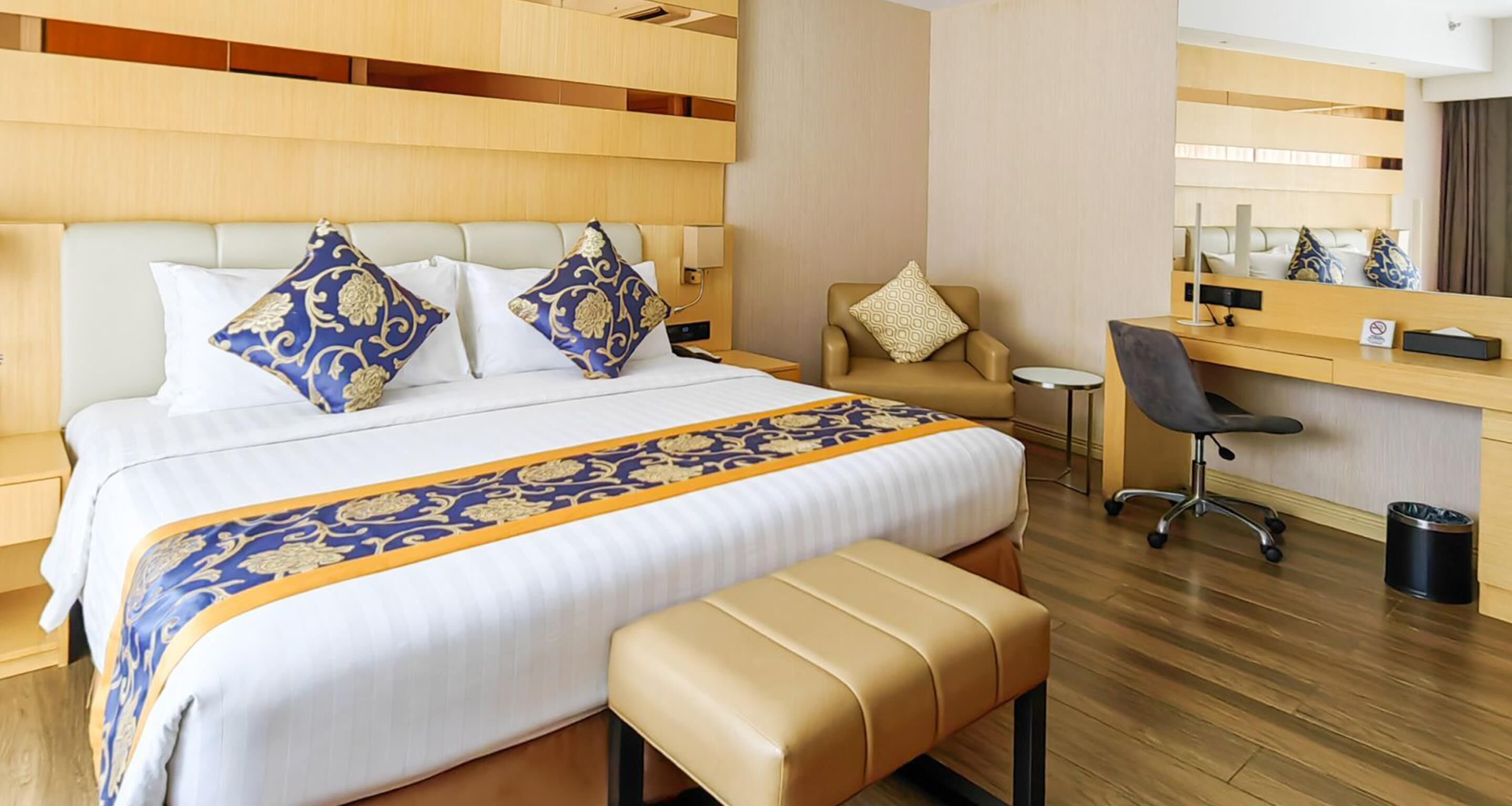 A hotel room with a large bed, a desk, a chair, and a bench.