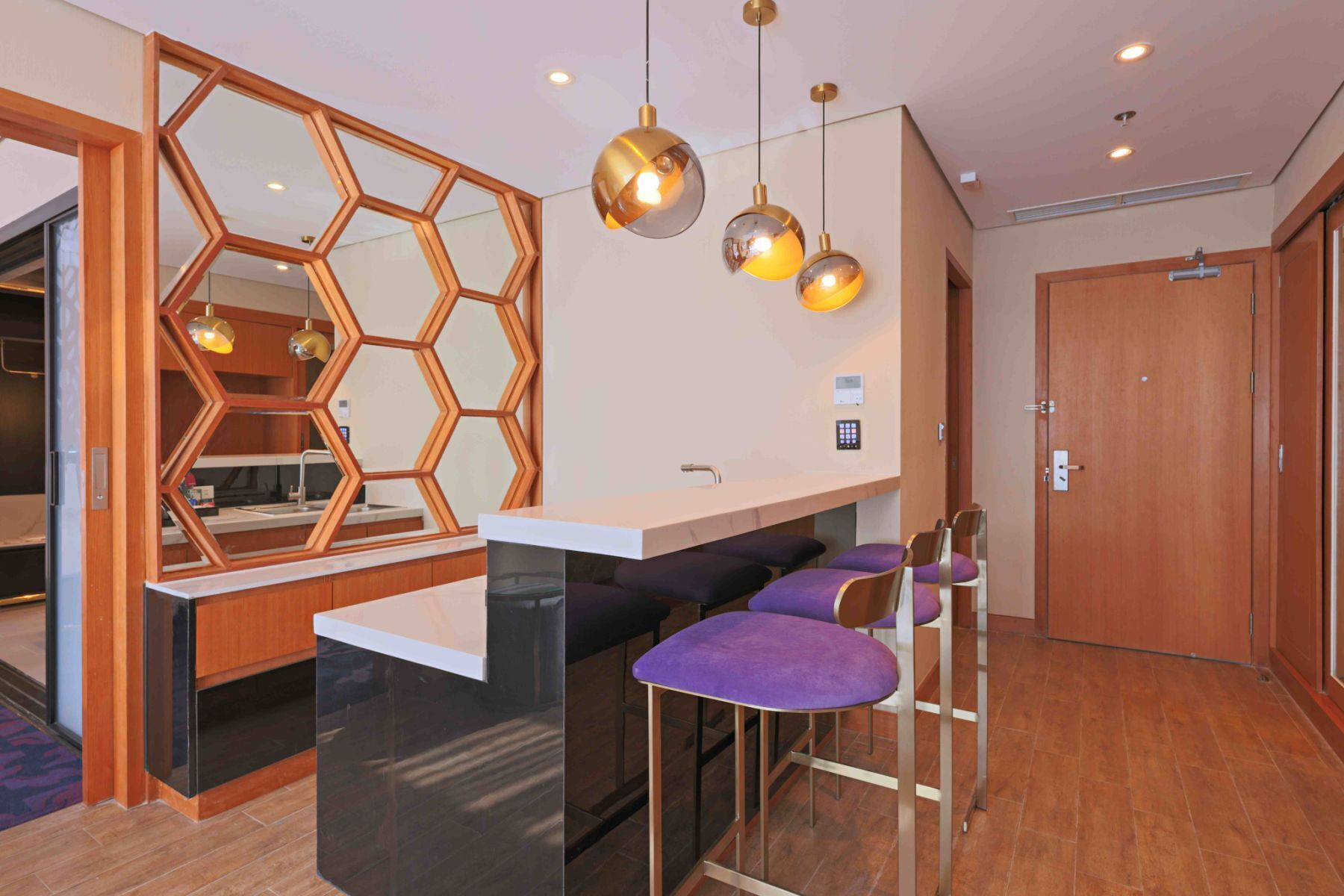 Una cocina moderna con una isla central, un espejo hexagonal e iluminación colgante.