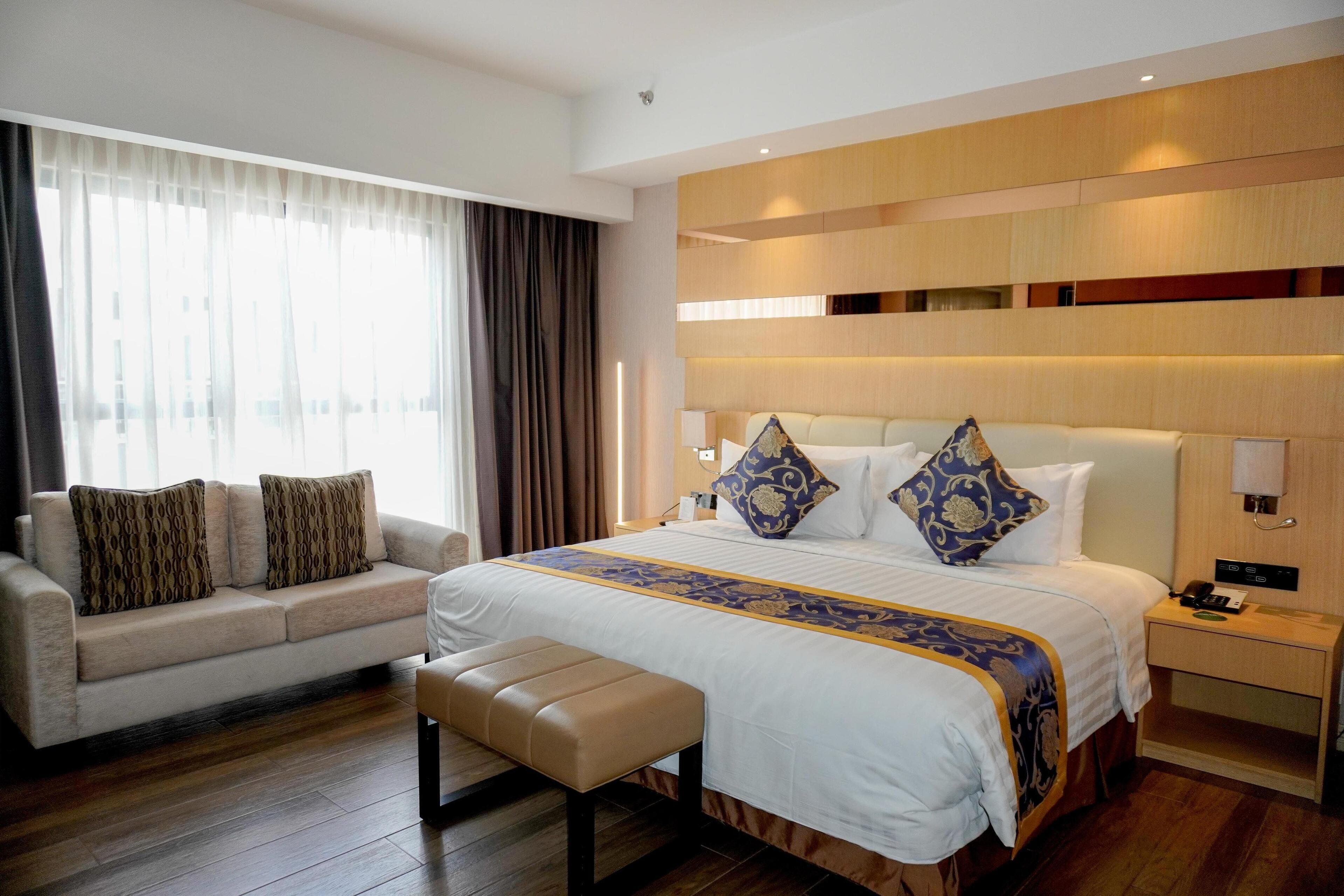 A hotel room with a large bed, a sofa, and a bench.