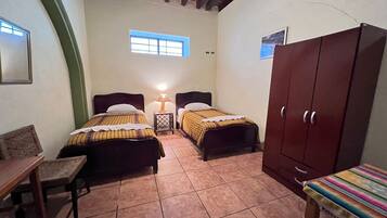 A small, cozy room with two beds, a wooden wardrobe, a small table, and a bench.