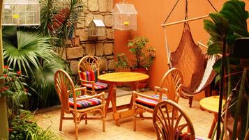 A cozy outdoor seating area with wicker chairs and a round table, surrounded by potted plants and a hammock.