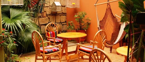 A cozy outdoor seating area with wicker chairs and a round table, surrounded by potted plants and a hammock.