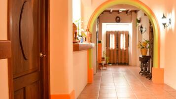 Un pasillo con puerta de madera, suelo de baldosas y un arco que da a una habitación.