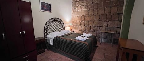 Un dormitorio con cama, armario, pared de piedra y una mesita.