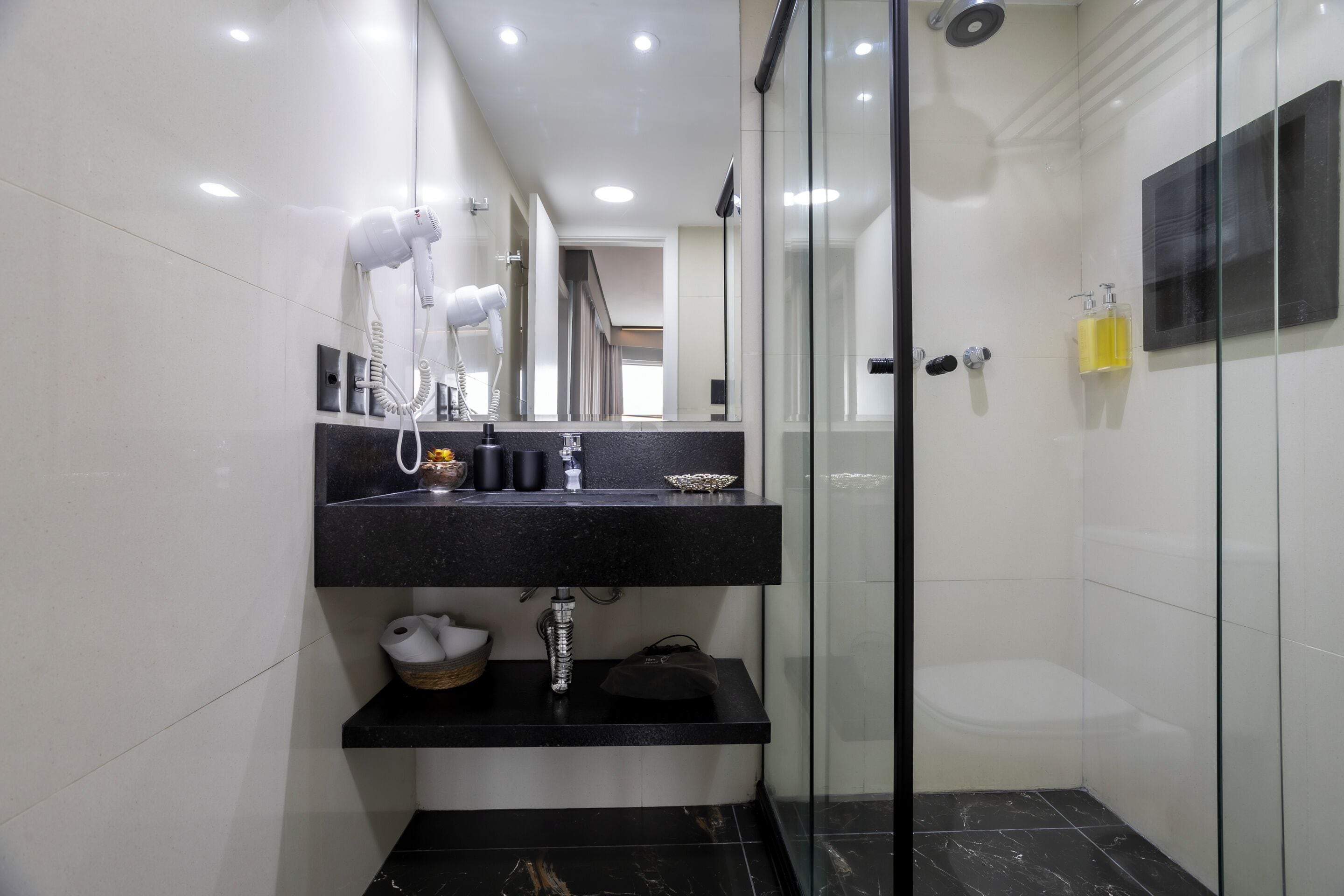 Un baño moderno con lavamanos de encimera negro, un secador de pelo y una ducha con mampara de vidrio.
