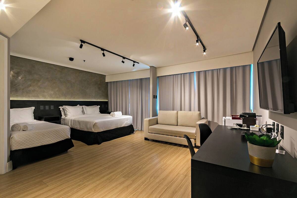Een moderne hotelkamer met twee bedden, een slaapbank, een bureau met een flatscreen televisie en een groot raam met gordijnen.