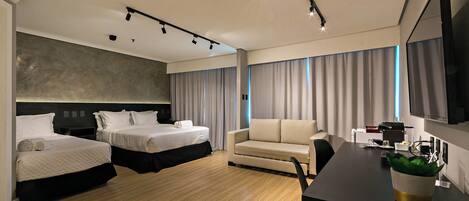 A modern hotel room with two beds, a sofa, a desk with a flat-screen TV, and a large window with curtains.