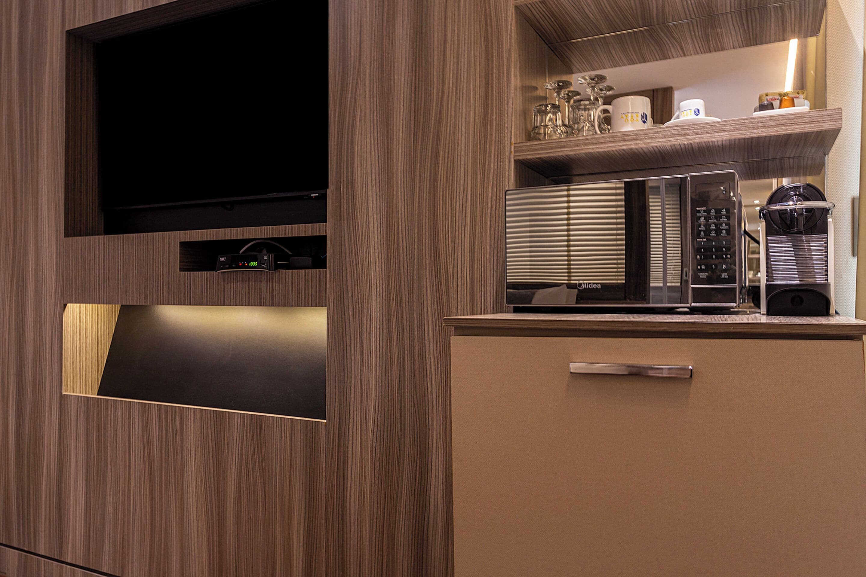 Een moderne keuken met een ingebouwde magnetron, koffieapparaat en een flatscreen televisie aan de wand.