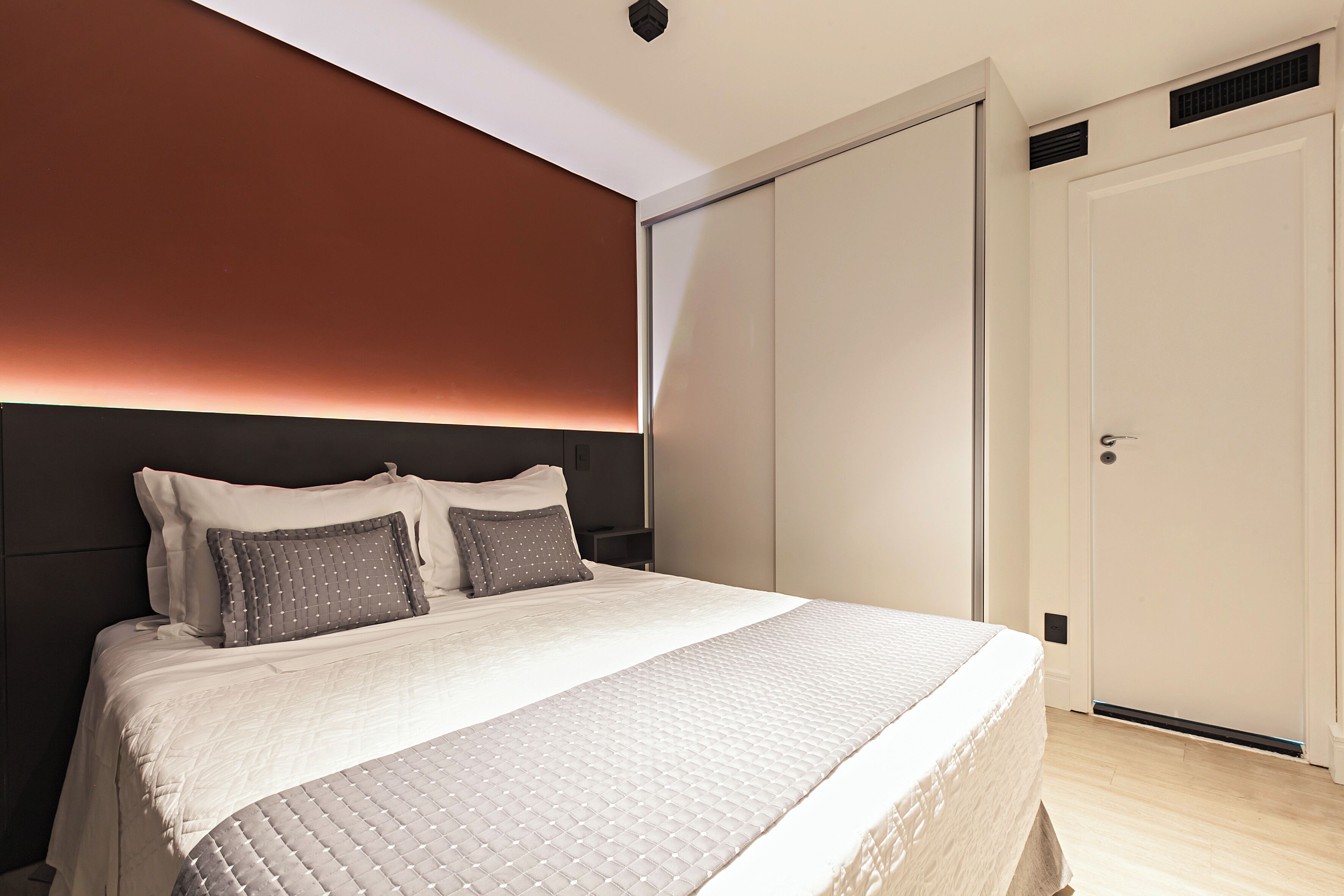 Una cama bien hecha con cabecera, una puerta cerrada y una pared de color claro.