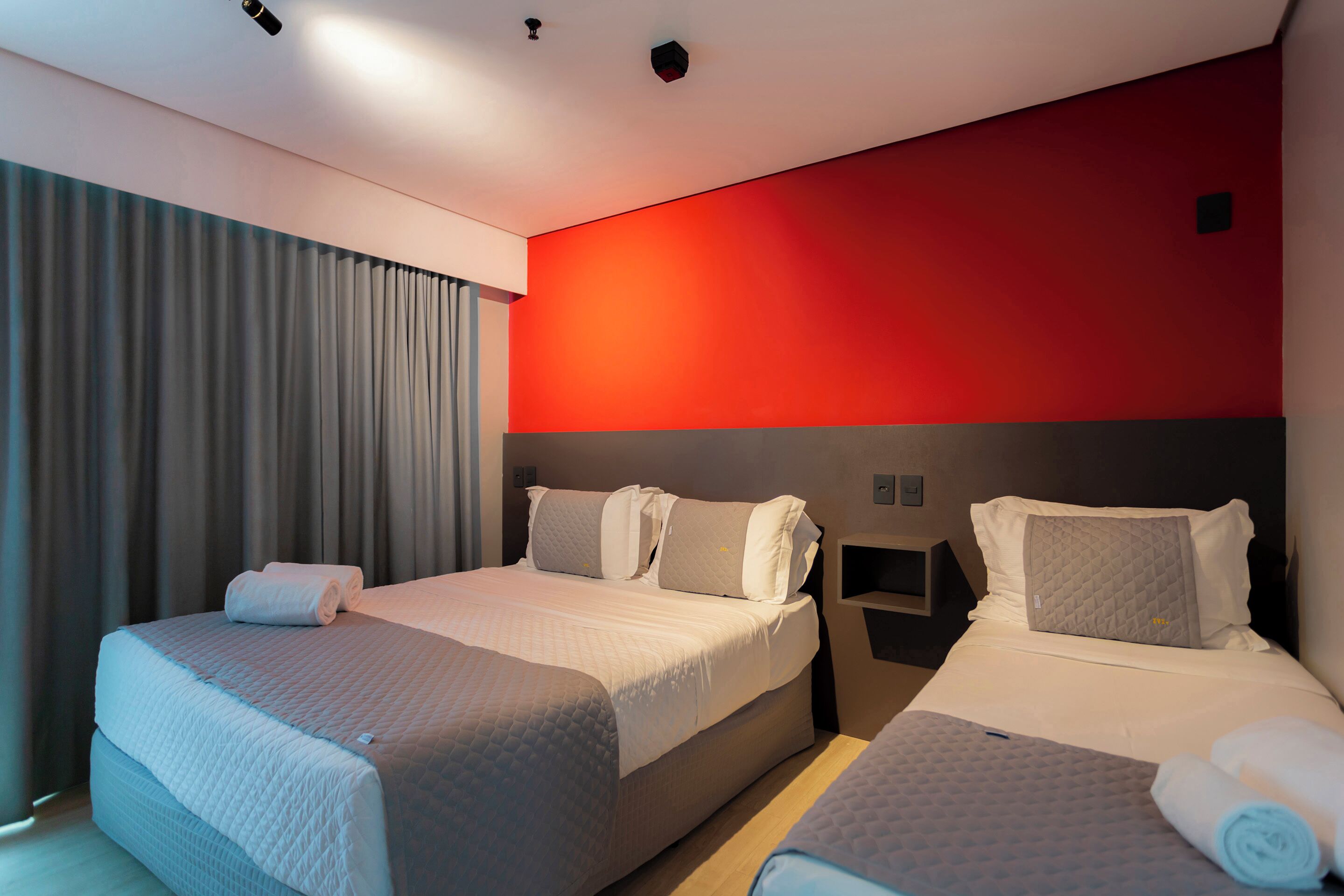Ein Hotelzimmer mit zwei Betten, einer roten Akzentwand und einem großen Fenster mit Vorhängen.