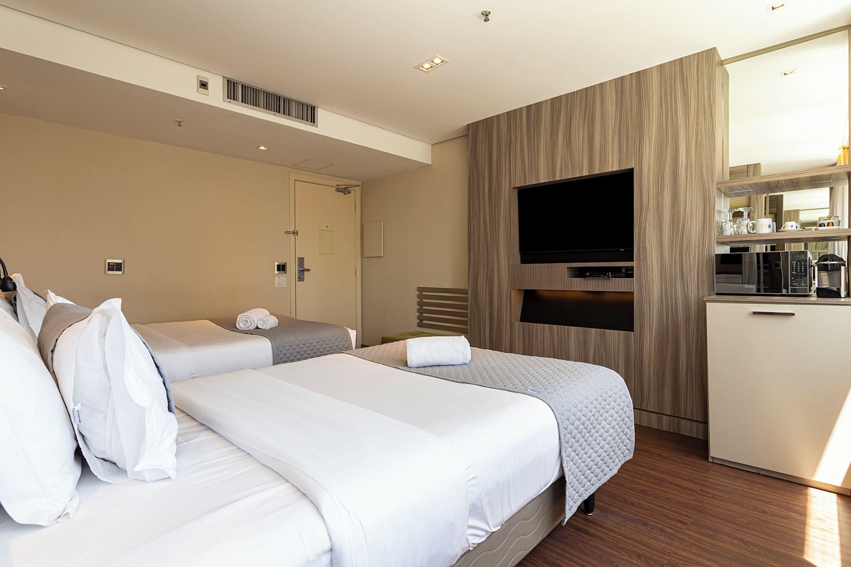 Habitación de hotel con dos camas, televisión, minibar y baño con toallero.