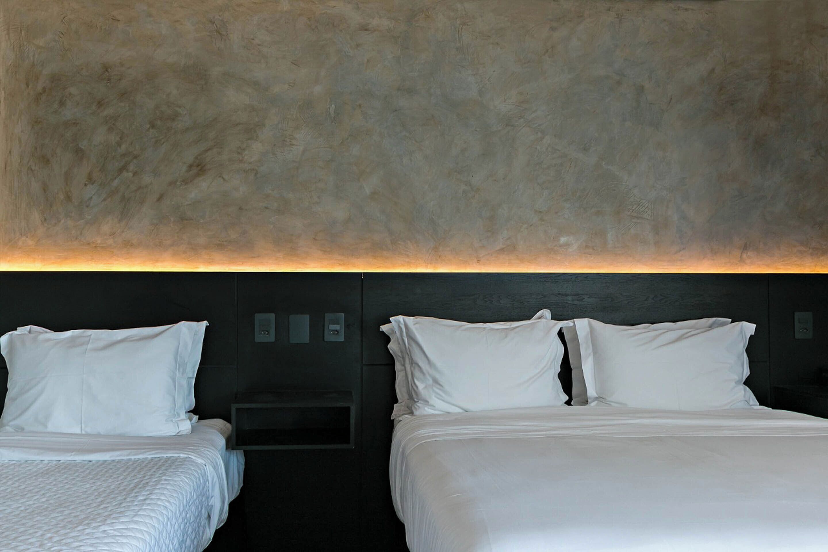 A hotel room with two beds, a dark wall, and a textured ceiling.