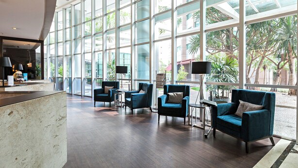 Eine geräumige Lobby mit großen Fenstern, einem Empfangstresen und mehreren blauen Sesseln.