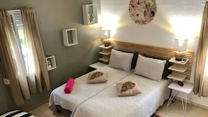 A bedroom with a bed, bedside tables, a wall clock, and a window with curtains.
