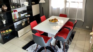 A modern dining area with a white table, red and grey chairs, a black and white bookshelf, and a decorative lamp.