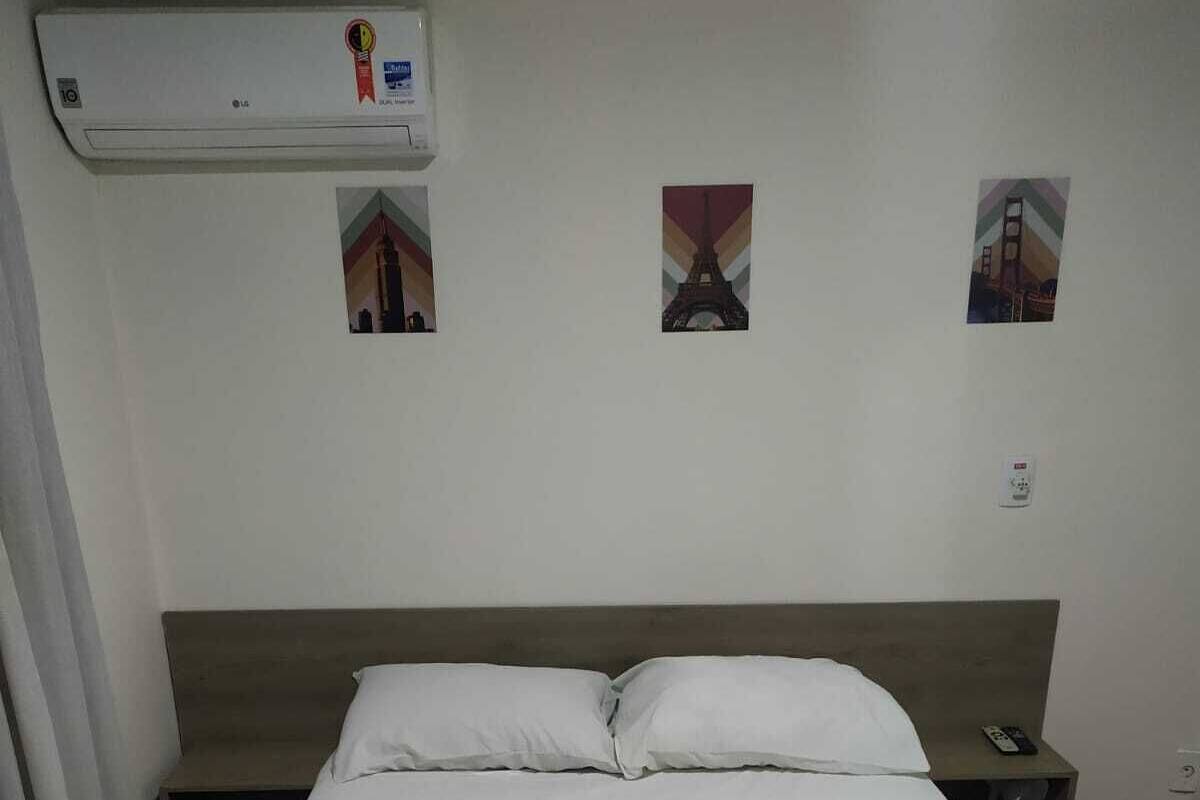 A hotel room with a bed, a nightstand, a phone, and a wall-mounted air conditioner.