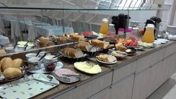 A buffet with various food items and beverages, including bread, pastries, and fruit.