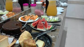 A buffet with various food items including a chocolate cake, watermelon slices, and different types of bread.