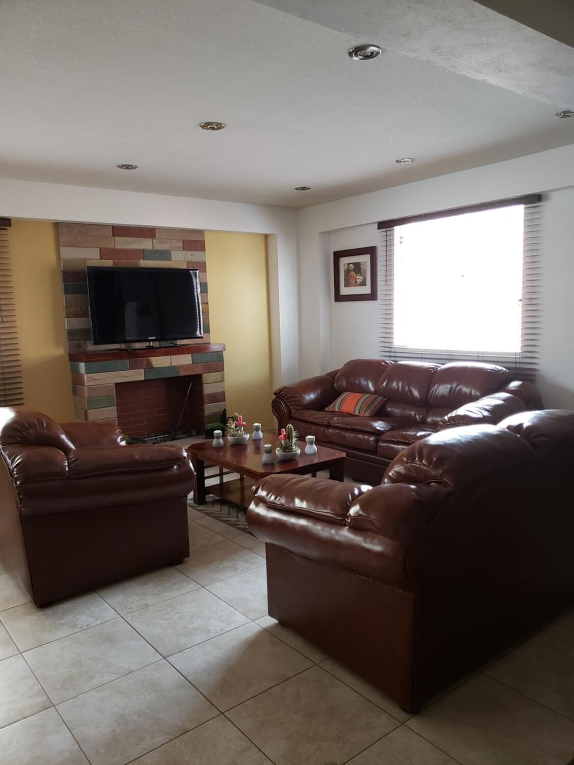 A living room with a fireplace, leather sofas, a coffee table, and a flat-screen TV mounted on a multicolored wall.