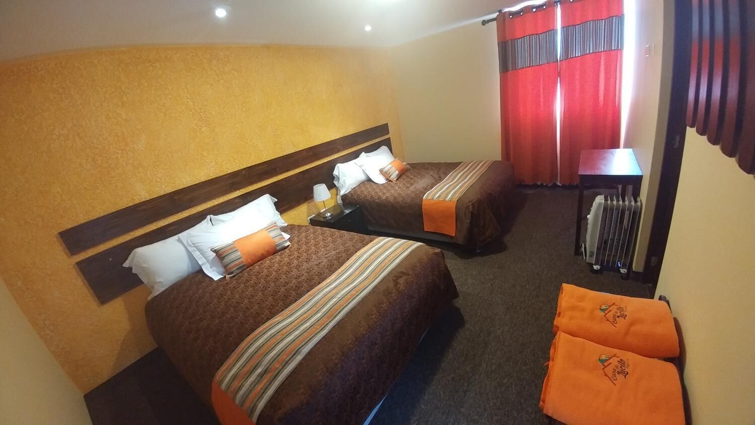 Een hotelkamer met twee bedden, elk voorzien van een streepjesbeddegoed en kussens. Er staat een klein tafeltje met een lamp en een koffer.