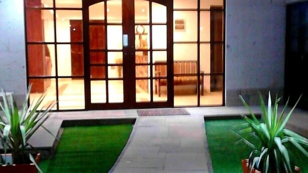 A modern building entrance with a glass door, a tiled pathway, and green artificial grass on either side. - Casa de Lucila (Chivay)