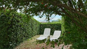 A garden with two white lounge chairs under a tree, surrounded by dense green foliage. - N107 - Numana, large three-room apartment with garden and two bathrooms (Numana)
