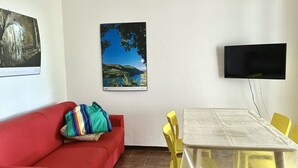A room with a red couch, a table with yellow chairs, a framed picture on the wall, and a flat-screen TV. - N107 - Numana, large three-room apartment with garden and two bathrooms (Numana)