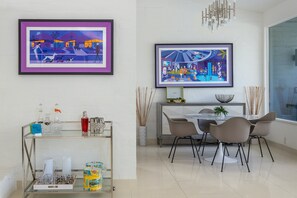 Un espace repas avec une table en verre, des chaises et une œuvre d’art encadrée au mur.