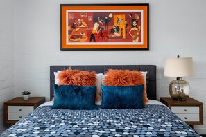 Une chambre à coucher avec un lit, deux tables de chevet, une œuvre d’art encadrée et une lampe.