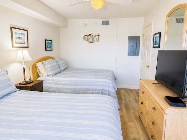 A bedroom with two beds, a television, a dresser, and a ceiling fan.