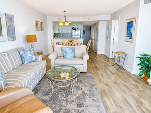A living room with a sofa, armchair, glass coffee table, and a rug.