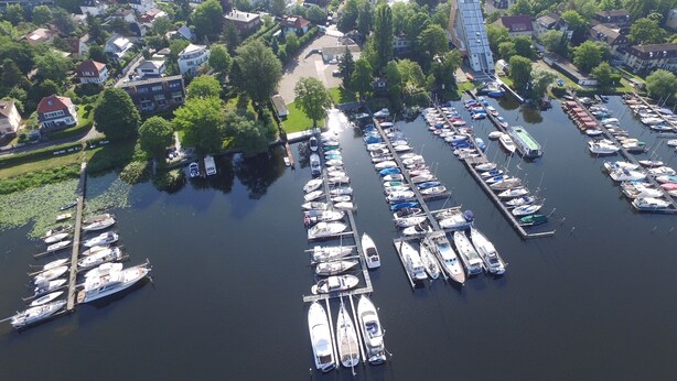 An aerial view of a marina with numerous boats docked, surrounded by residential buildings and greenery. - bunk by the water (Bezirk Spandau)