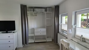 A room with a TV on a stand, a white dresser with drawers, a closet with hanging space, and a window with a view of greenery. - bunk by the water (Bezirk Spandau)